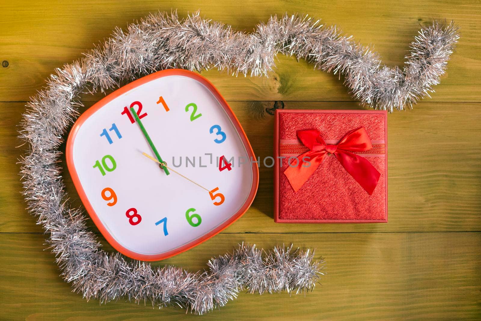 Decorated clock showing midnight and gift in beautiful red box on wooden table by Bazdar