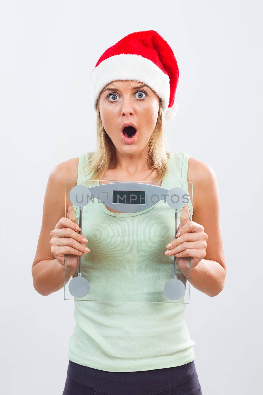 Portrait of woman with Santa hat in panic holding weight scale.