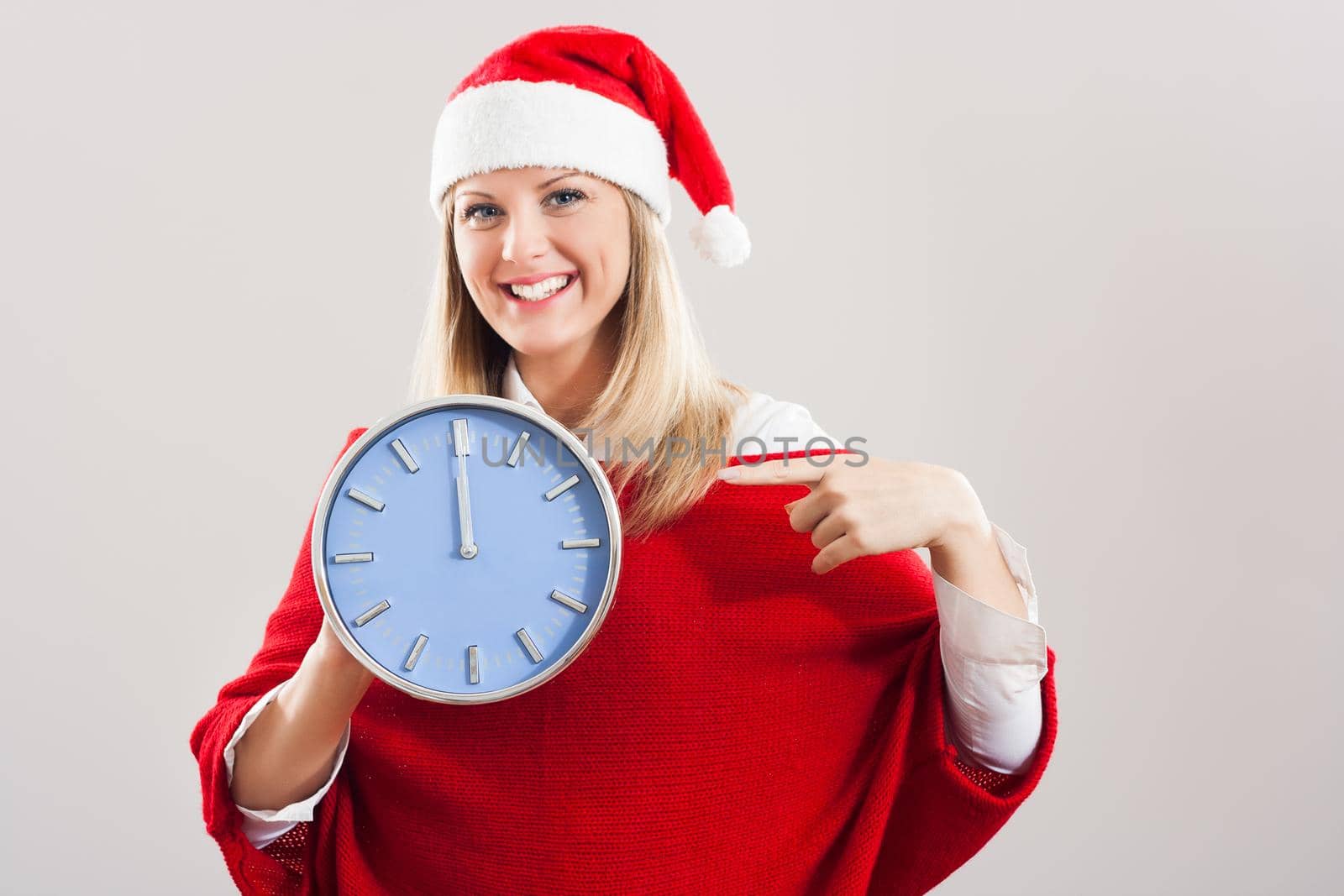 Happy young woman with Sant hat pointing at clock.
