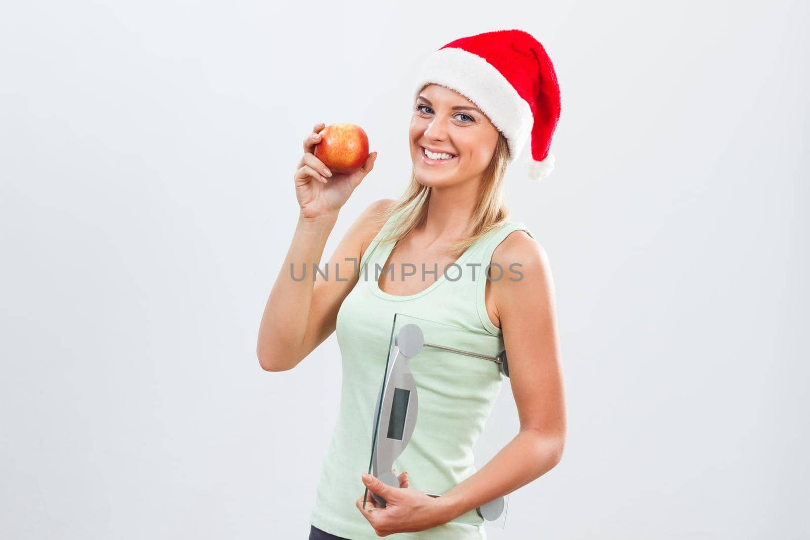 Happy woman with Santa hat holding apple and weight scale.