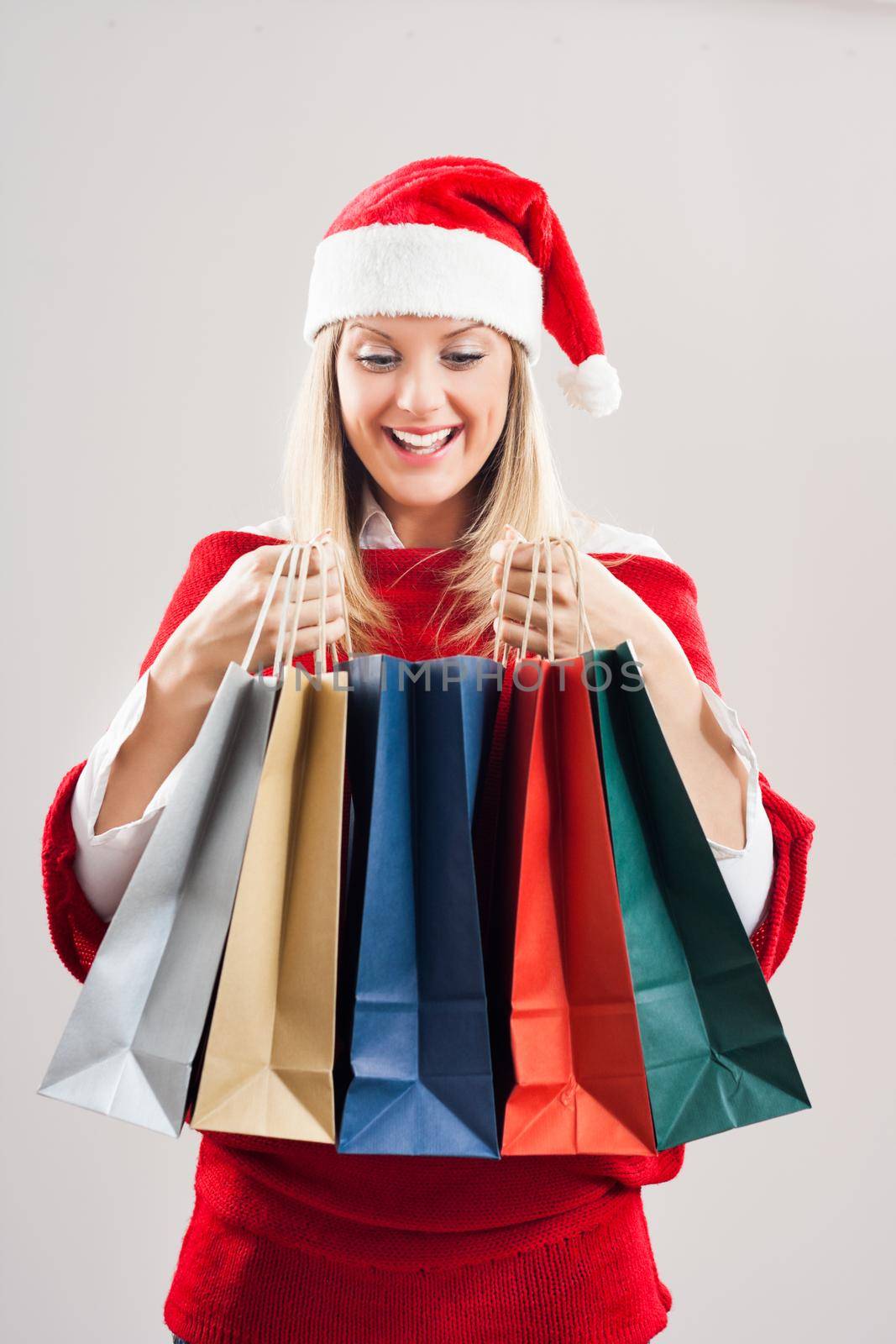 Image of beautiful young woman with Santa hat holding shopping bags.