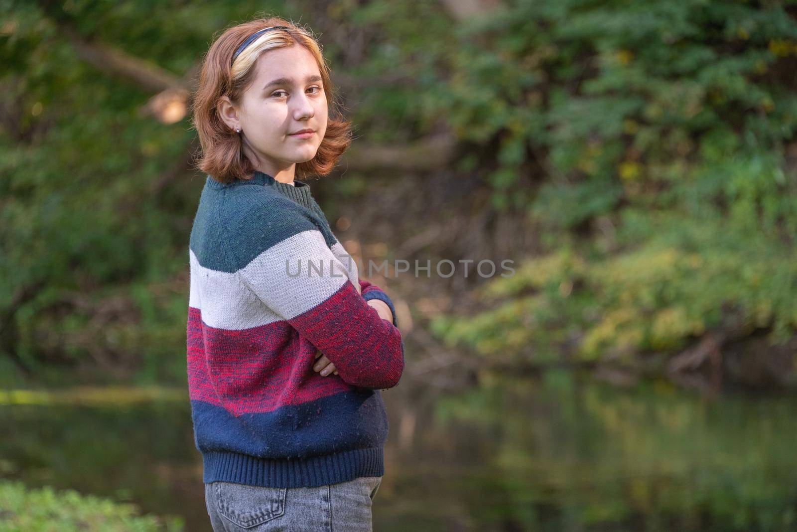 a teenage girl with a short haircut in a warm sweater portrait against the background of green nature in early autumn.