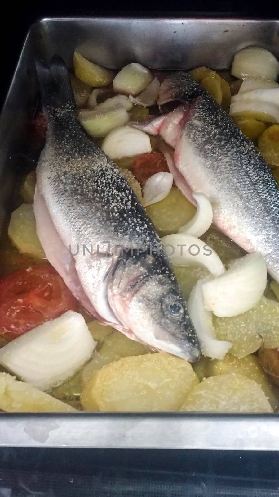 Preparation of roast fish with potatoes, tomatoes and onion in Spain