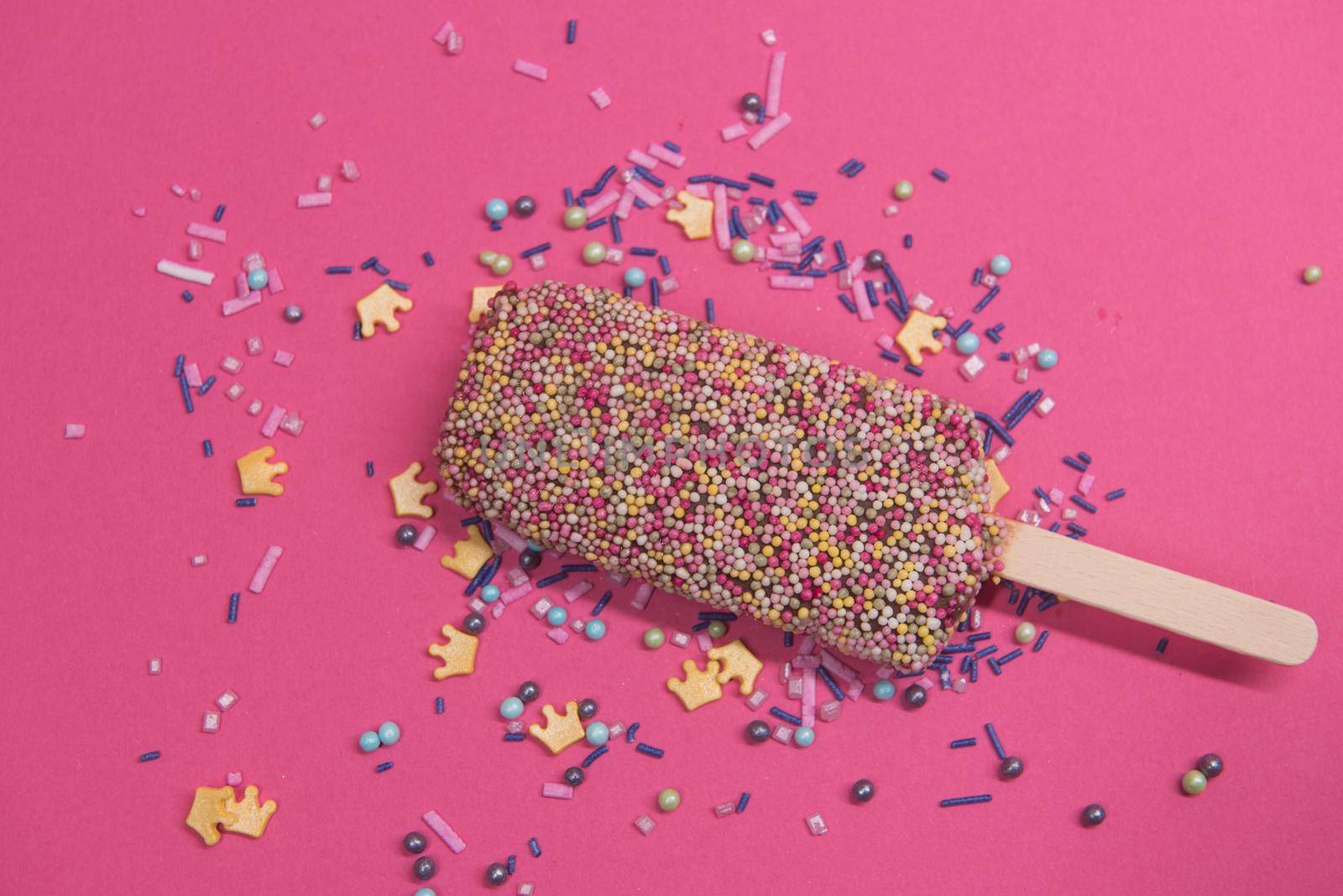 Ice cream on stick with colorful sprinkles over pink background