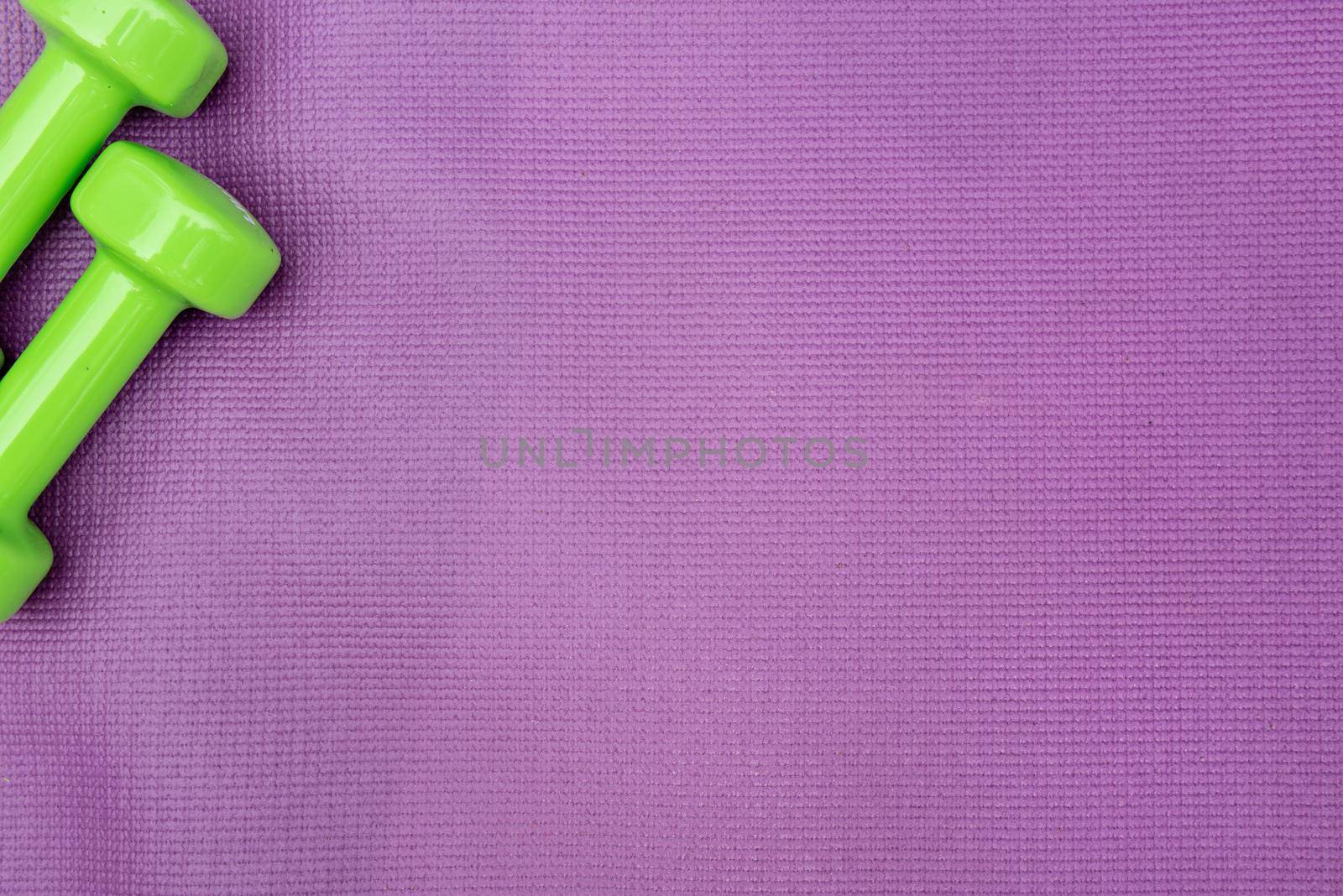 Ladie's dumbbells over purple fitness mat, top view. by anytka