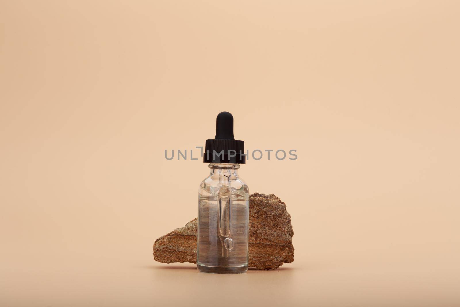 Skin serum bottle next to natural stone against bright beige background with copy space. Concept of luxury skin serum or oil for anti aging daily treatment