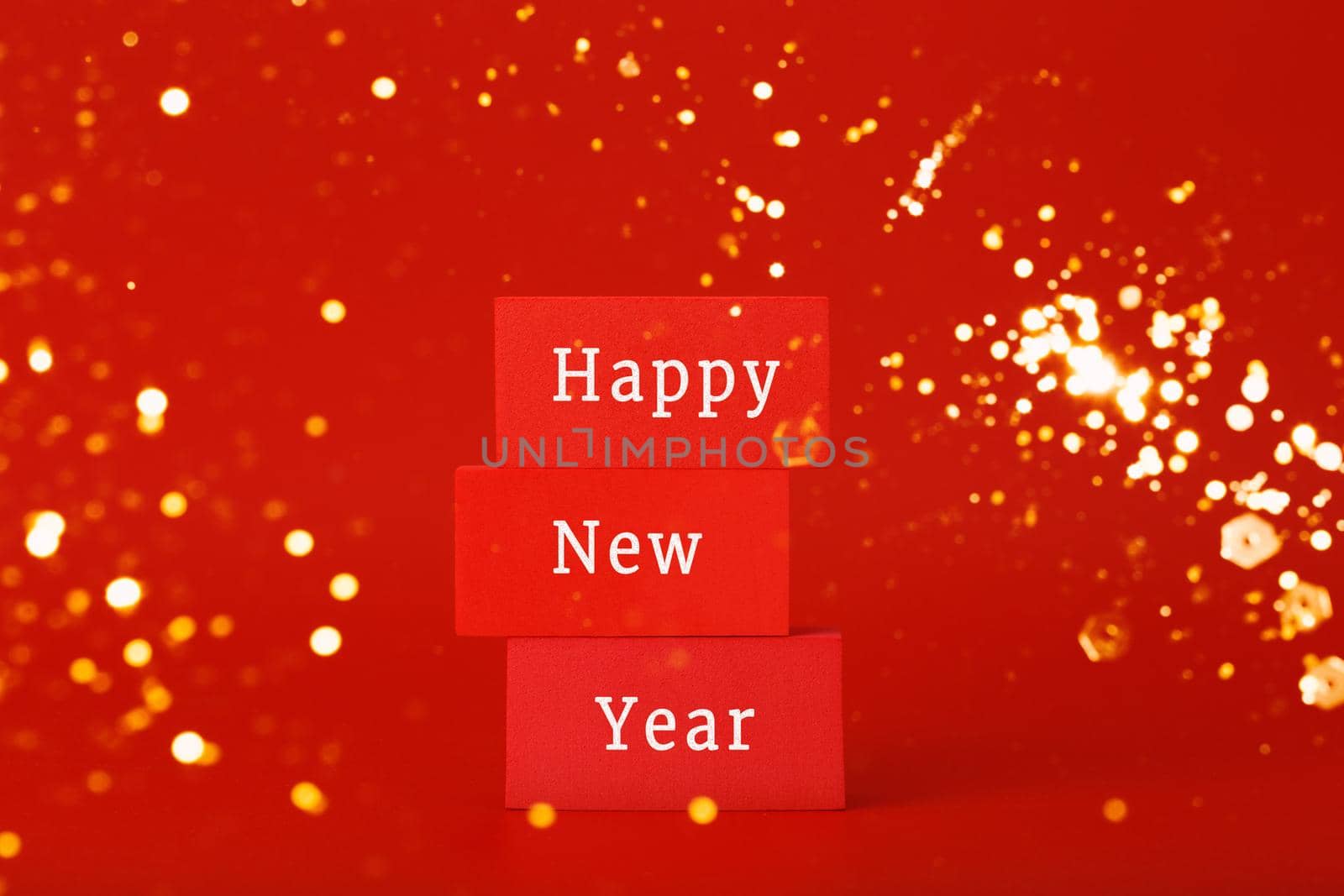 Happy New Year red minimal trendy concept. Modern festive composition with red toy blocks with written Happy New Year text against red background with golden bokeh