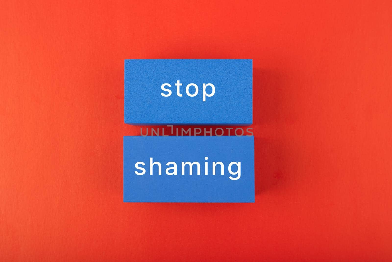 Stop shaming concept. Minimal flat lay with stop shaming inscription on blue rectangles on saturated red background. 