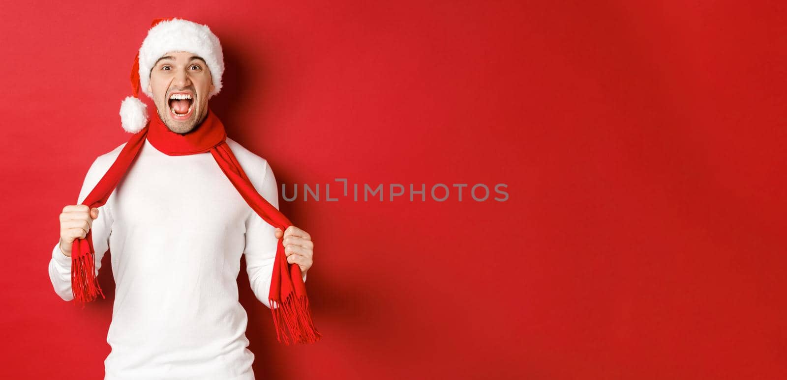 Image of angry adult man hate christmas, wearing scarf and santa hat, yelling distressed, standing mad over red background by Benzoix
