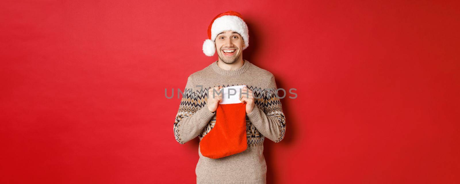 Concept of winter holidays, new year and celebration. Image of surprised and happy man receiving gift from secret santa inside christmas stocking bag, open gift and looking thankful.