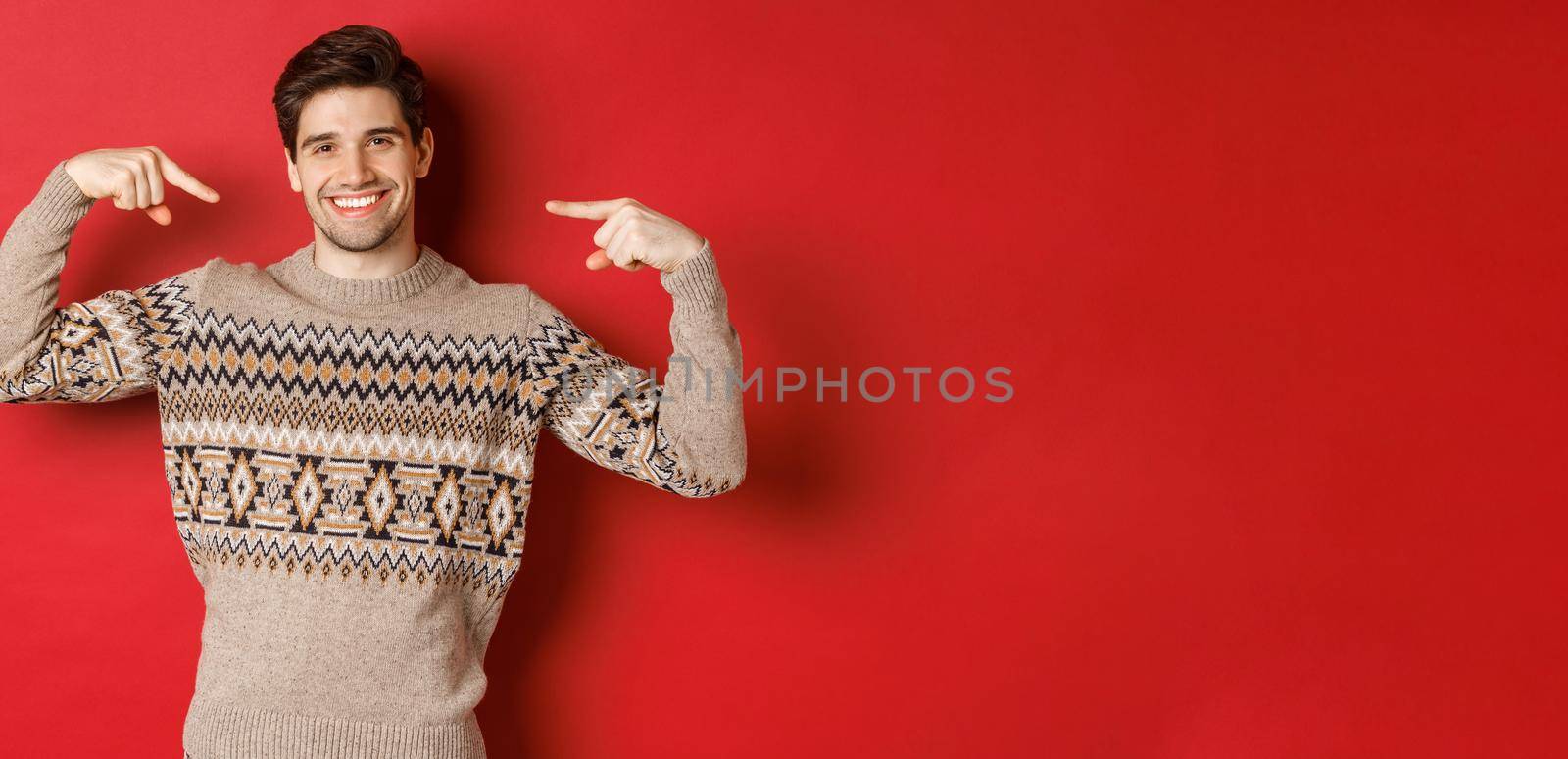 Concept of christmas celebration, winter holidays and lifestyle. Image of happy handsome man in xmas sweater pointing at himself and smiling, being secret santa, standing over red background by Benzoix