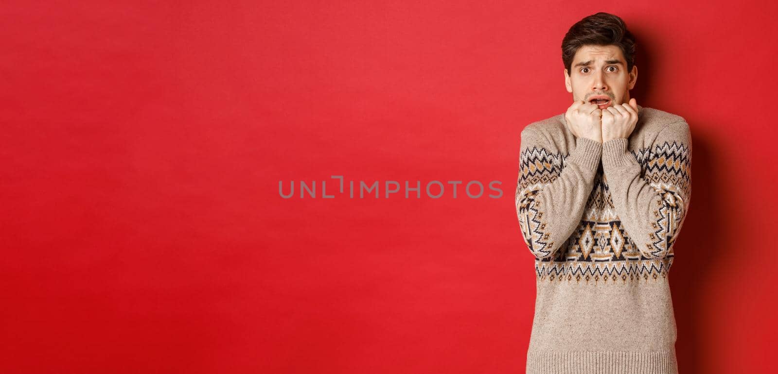 Portrait of scared and timid man in christmas sweater, looking frightened, watching something scary on new year, standing over red background by Benzoix