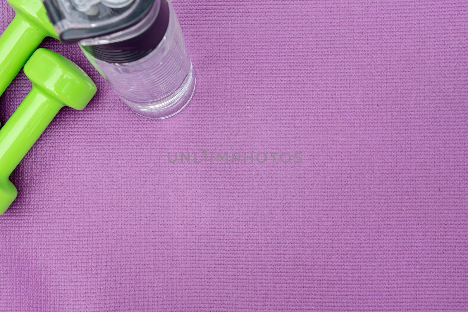 Ladie's dumbbells and water bottle over purple fitness mat, top view. Sport concept