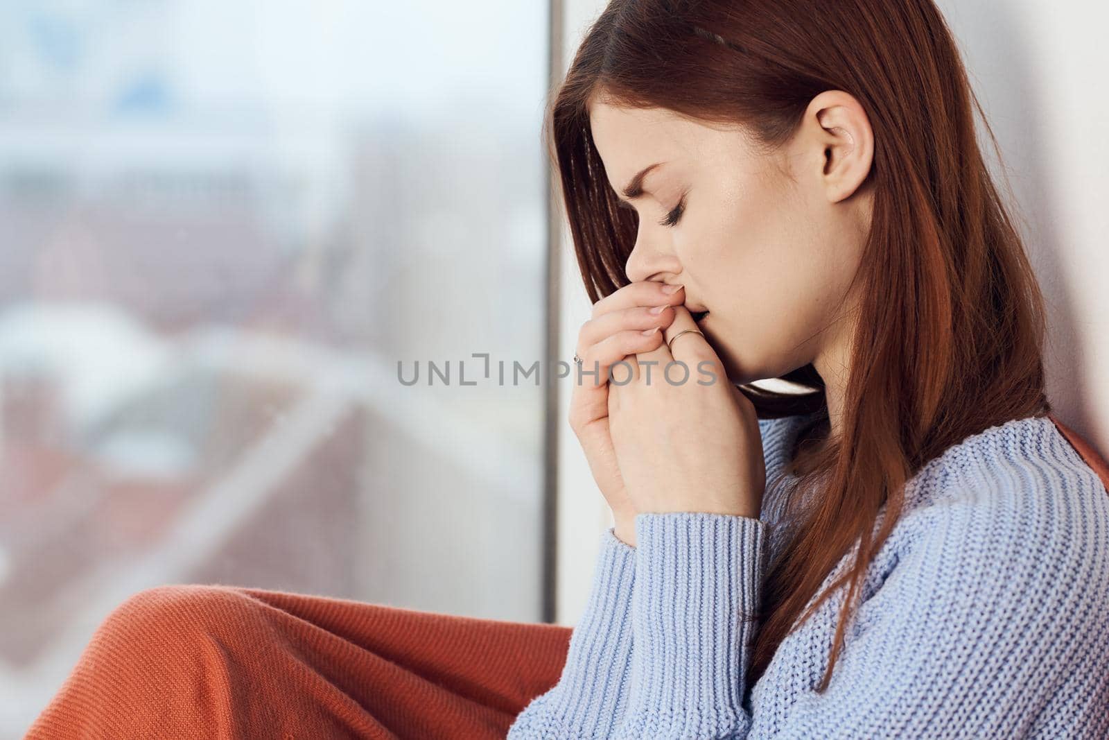 woman with sad expression sits by the window with a plaid. High quality photo