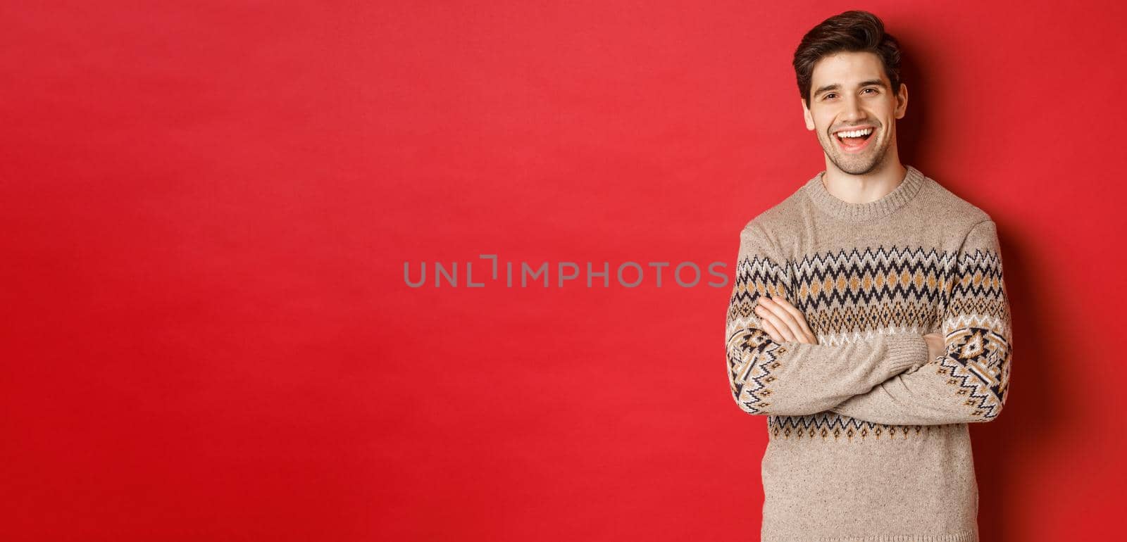 Portrait of cheerful, attractive man in christmas sweater, laughing and smiling, celebrating new year and winter holidays, standing over red background by Benzoix