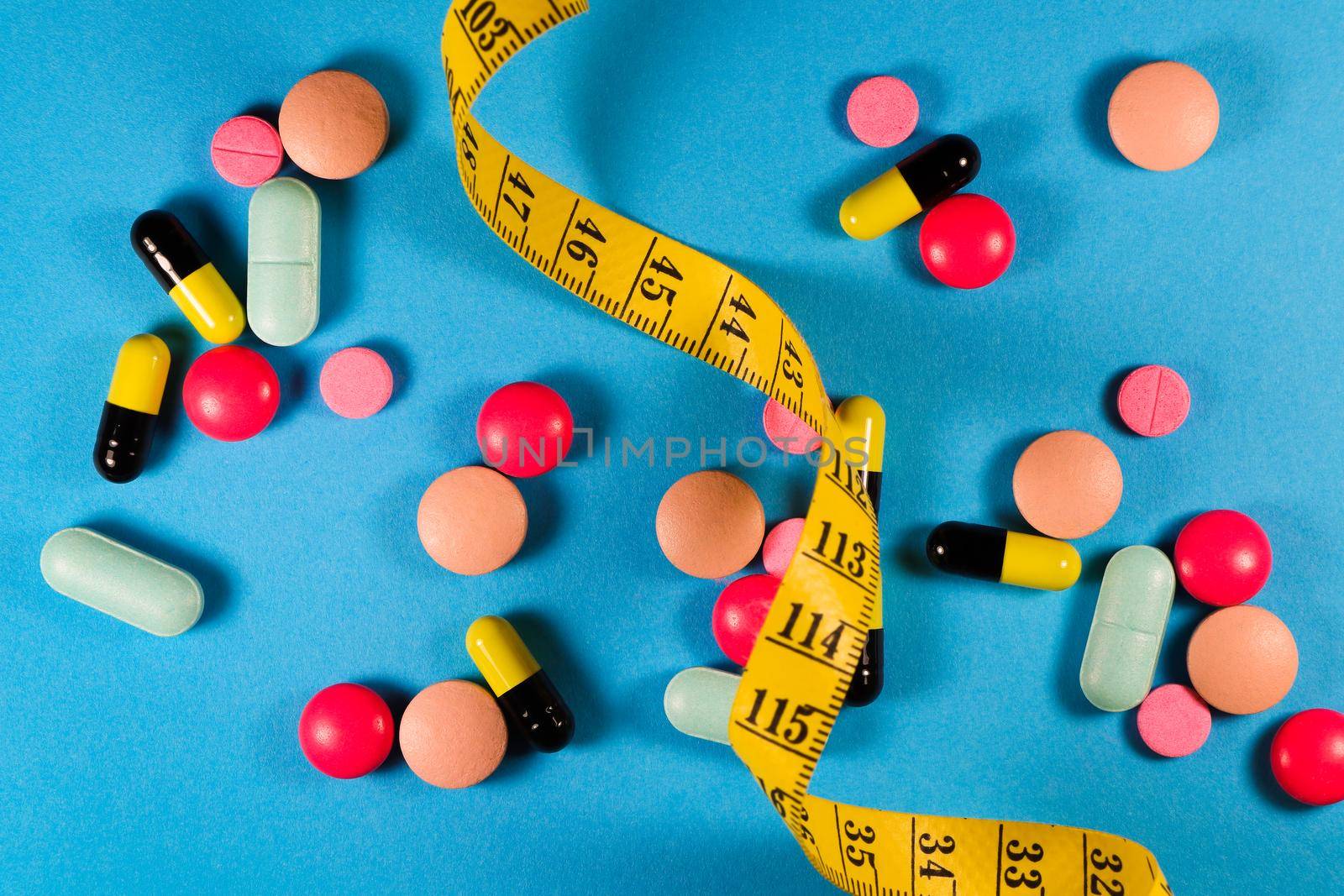 Yellow tape measure with a variety of weight loss medication on blue background