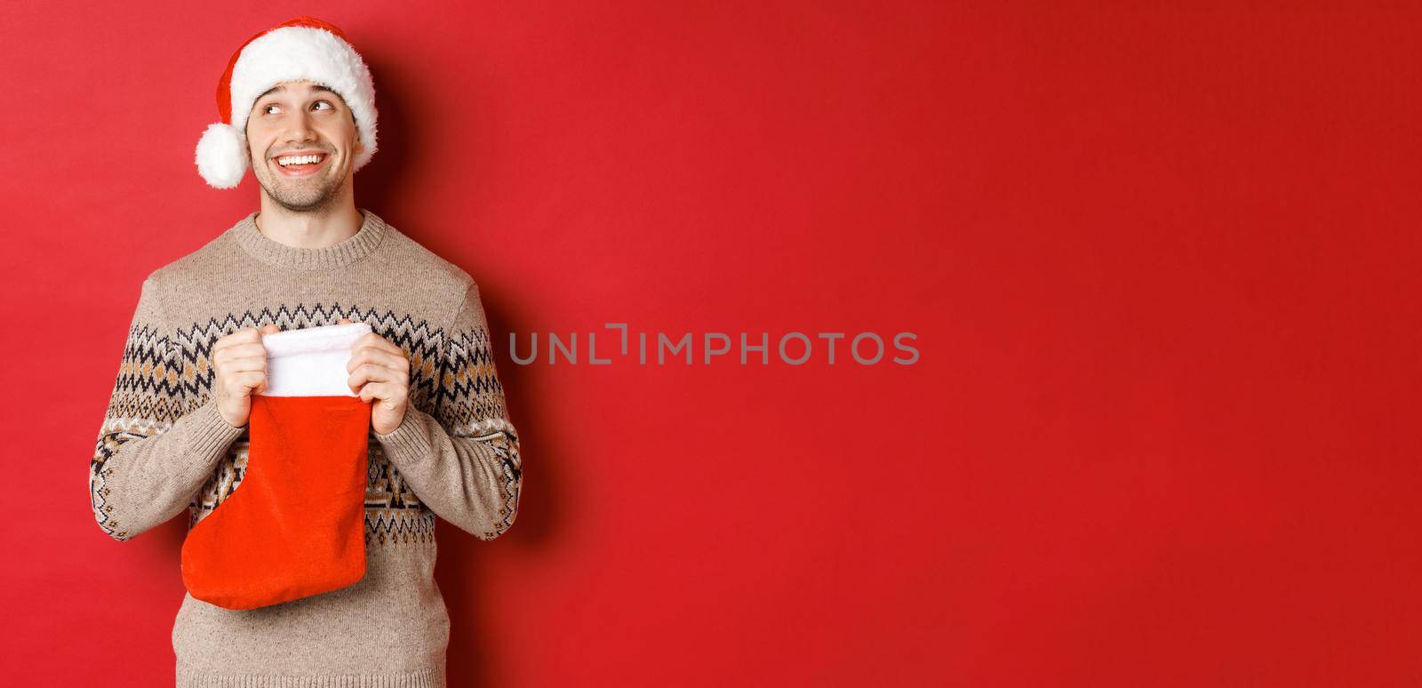 Concept of winter holidays, new year and celebration. Image of surprised and happy man receiving gift from secret santa inside christmas stocking bag, open gift and looking thankful by Benzoix