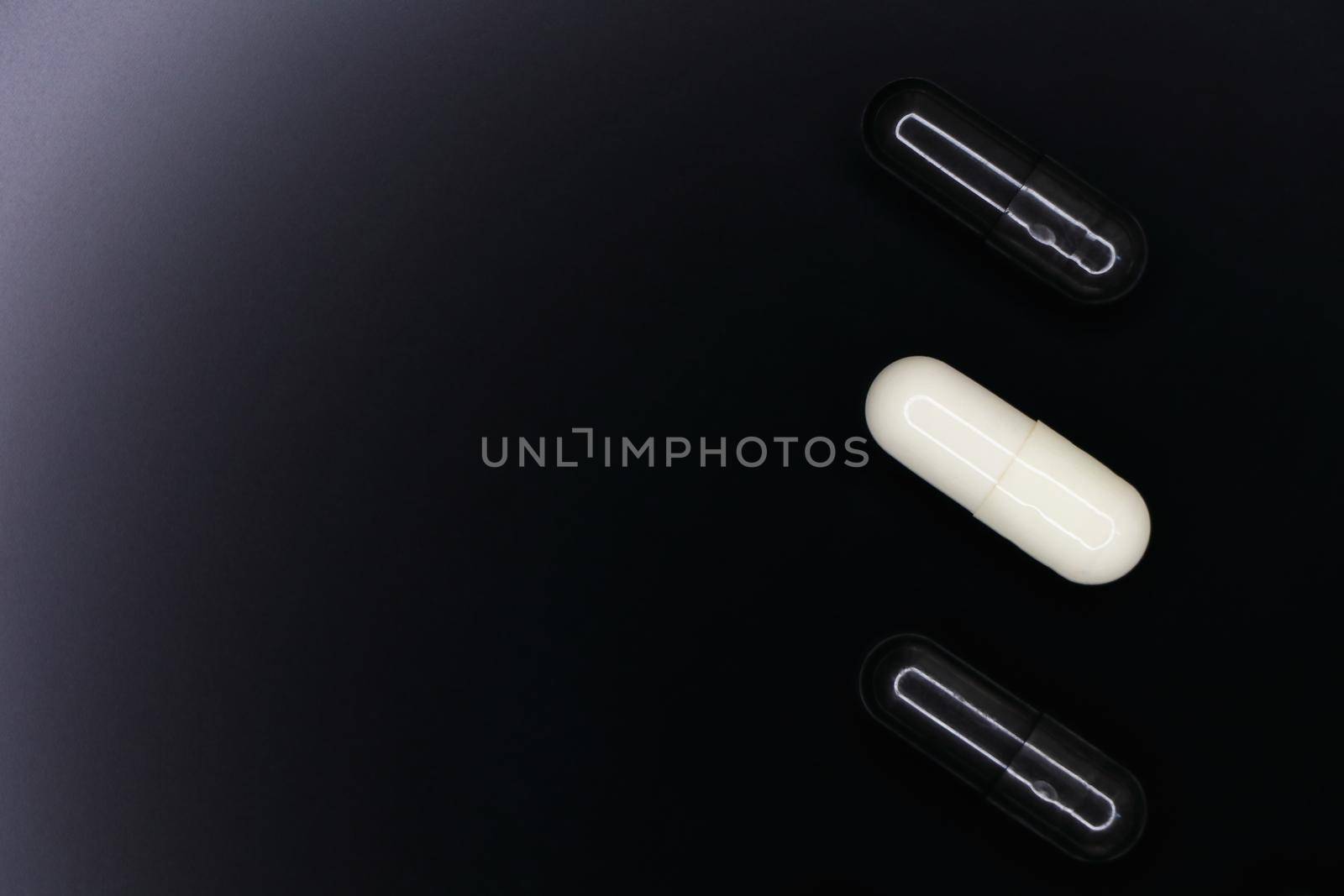 Black and white gel pill capsules layout on smooth black background