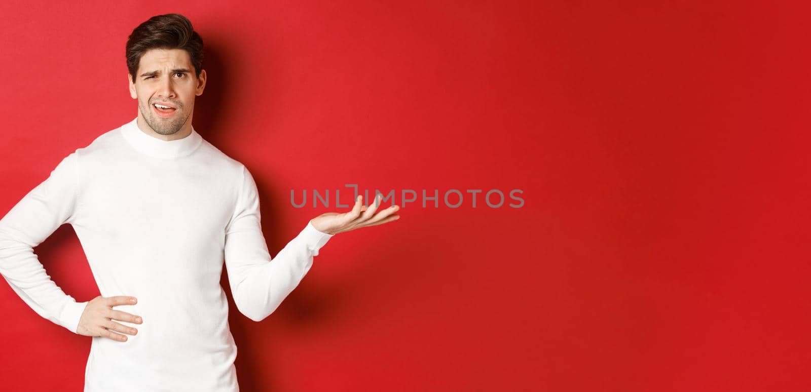 Portrait of confused and displeased man, complaining about something, looking with dismay, standing over red background.