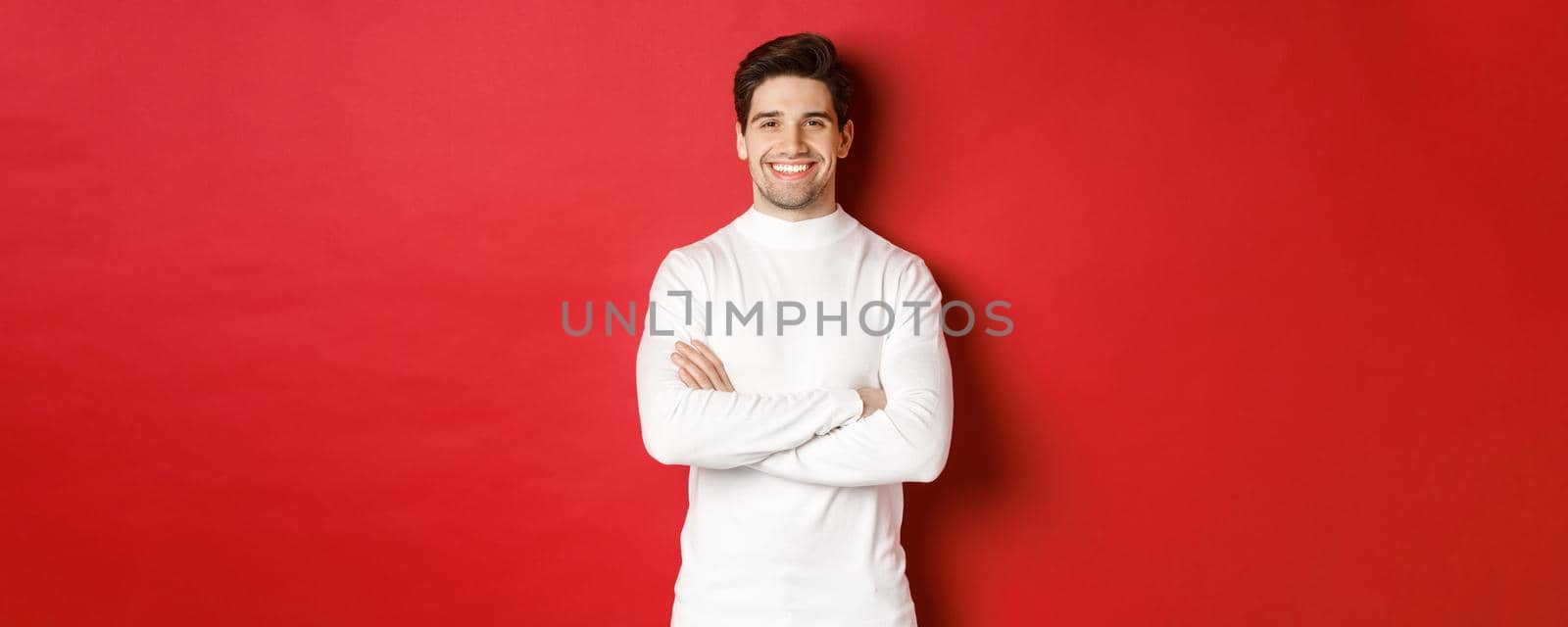 Concept of winter holidays, christmas and lifestyle. Portrait of confident good-looking man with bristle, wearing white sweater, cross arms on chest and smiling satisfied by Benzoix
