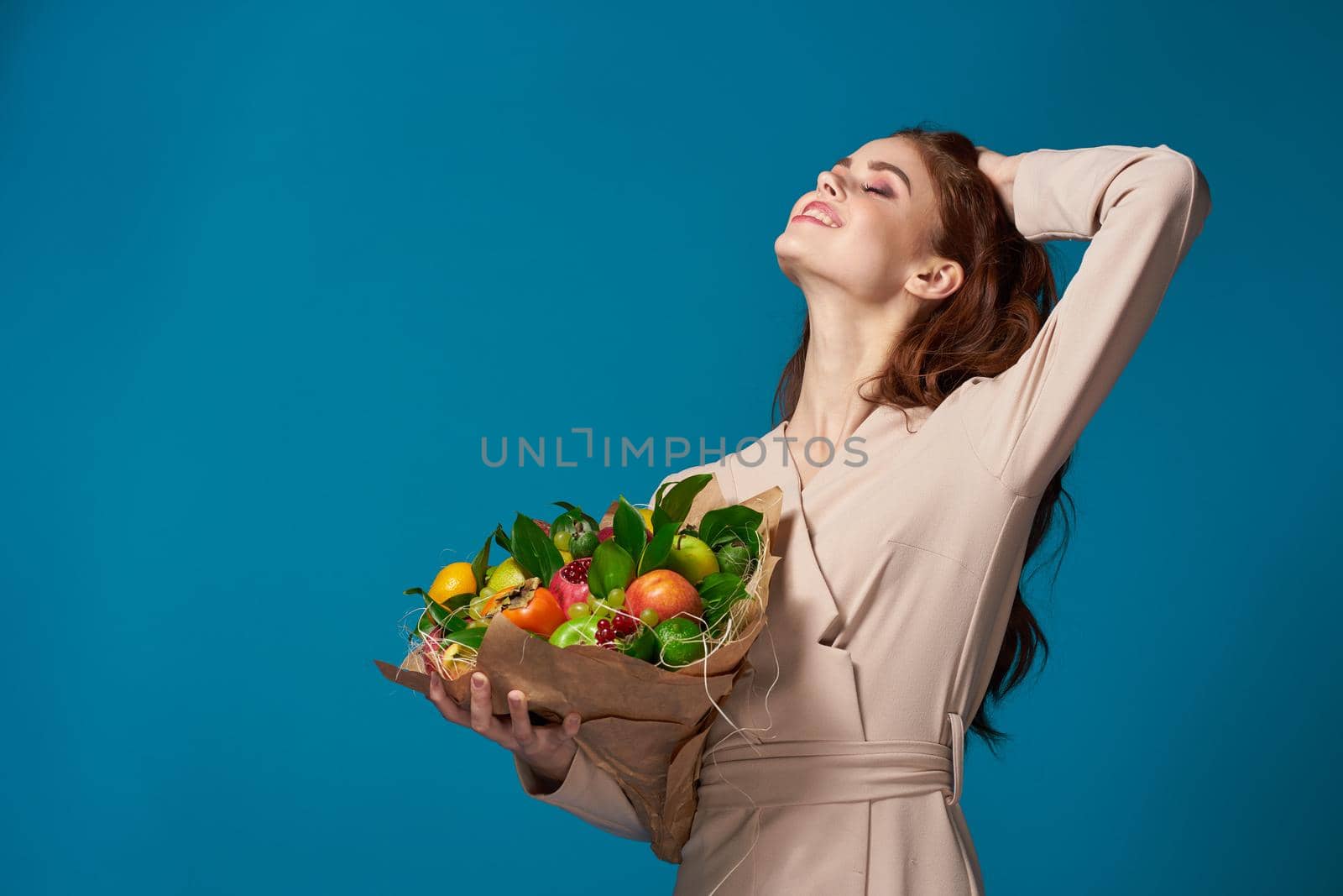 beautiful woman beige coat fruit bouquet in hands blue background. High quality photo