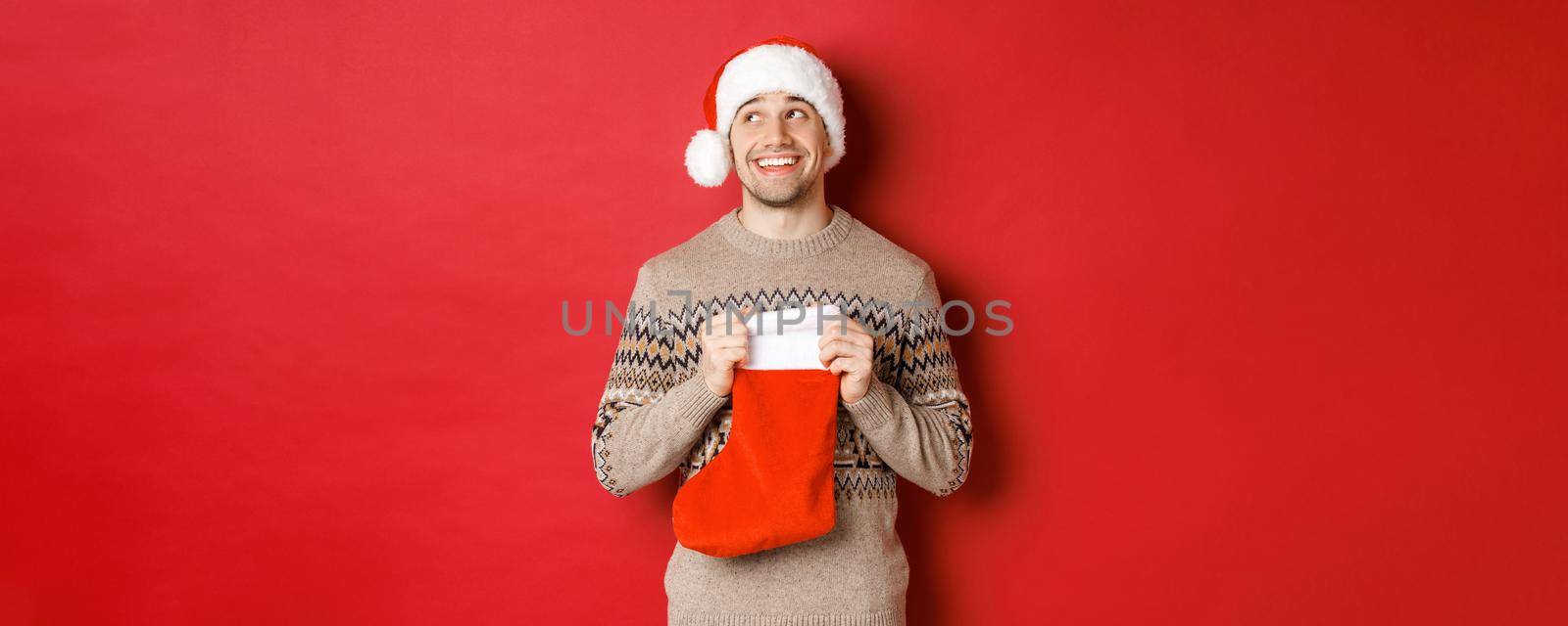 Concept of winter holidays, new year and celebration. Image of surprised and happy man receiving gift from secret santa inside christmas stocking bag, open gift and looking thankful.