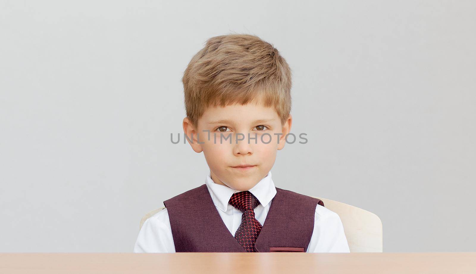 Serious boy sits at the desk in a vest with a tie . High quality photo