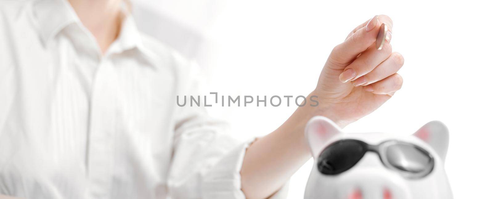 A woman's manicured hand dropping a coin into a piggy bank isolated on white. High quality photo