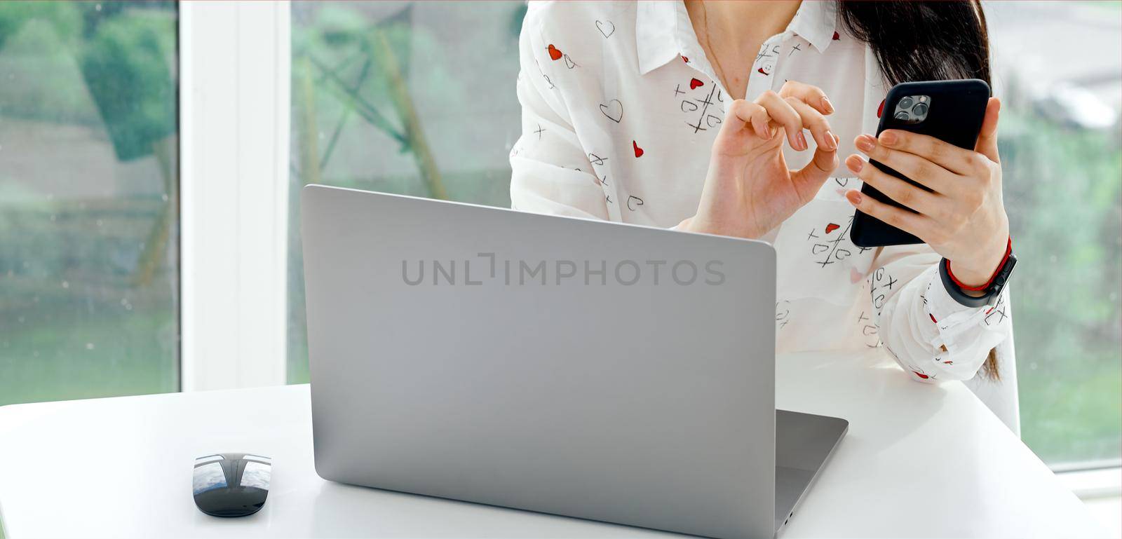 Woman working behind laptop checks phone white table . High quality photo