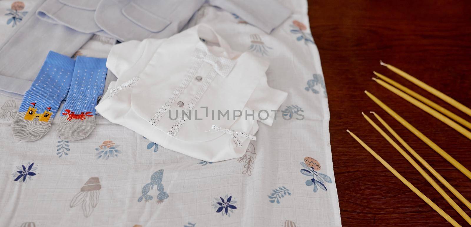 clothes for the baby on the diaper on a wooden table next to the candles of the christening . High quality photo
