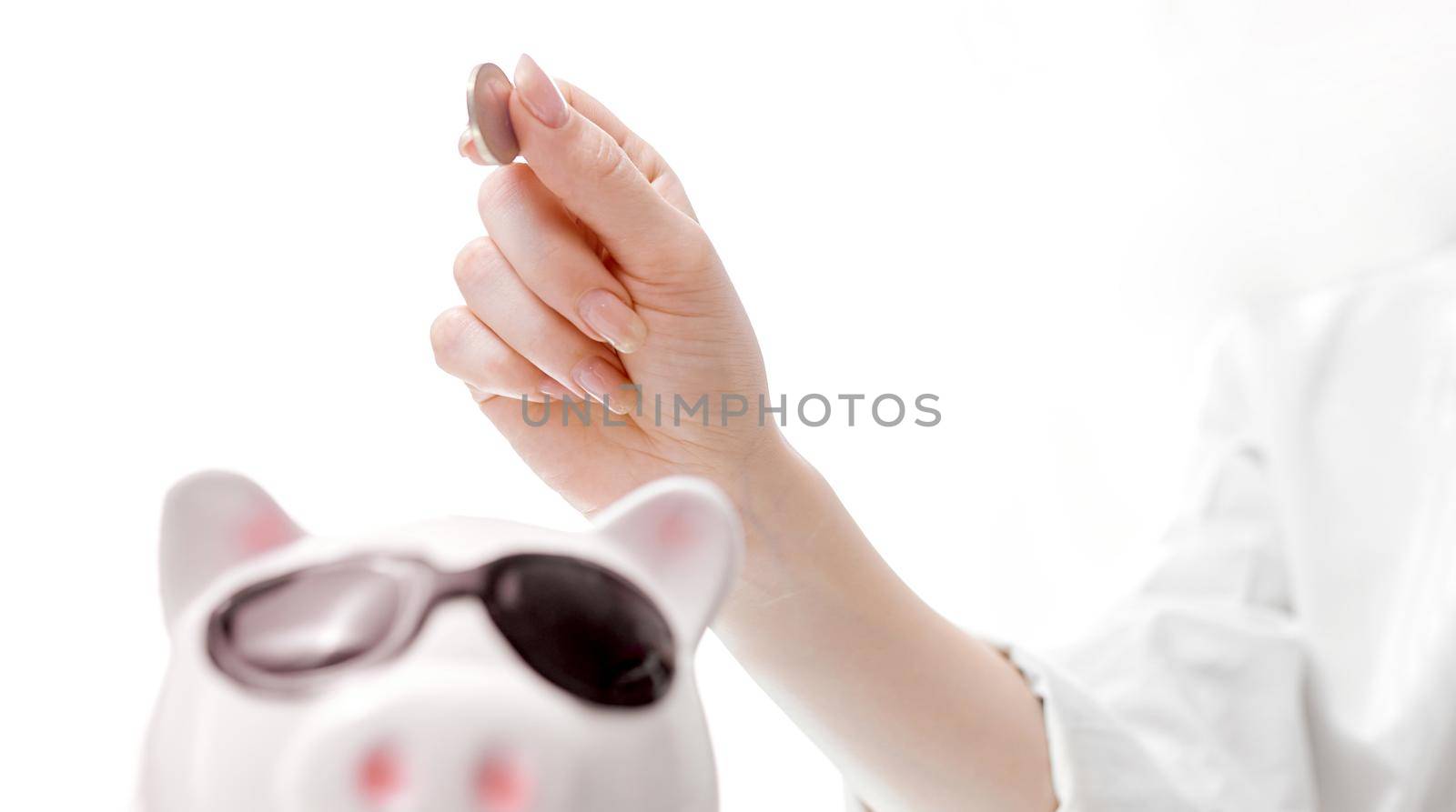 women's hand from top to bottom puts a coin in the piggy bank pig with glasses. High quality photo