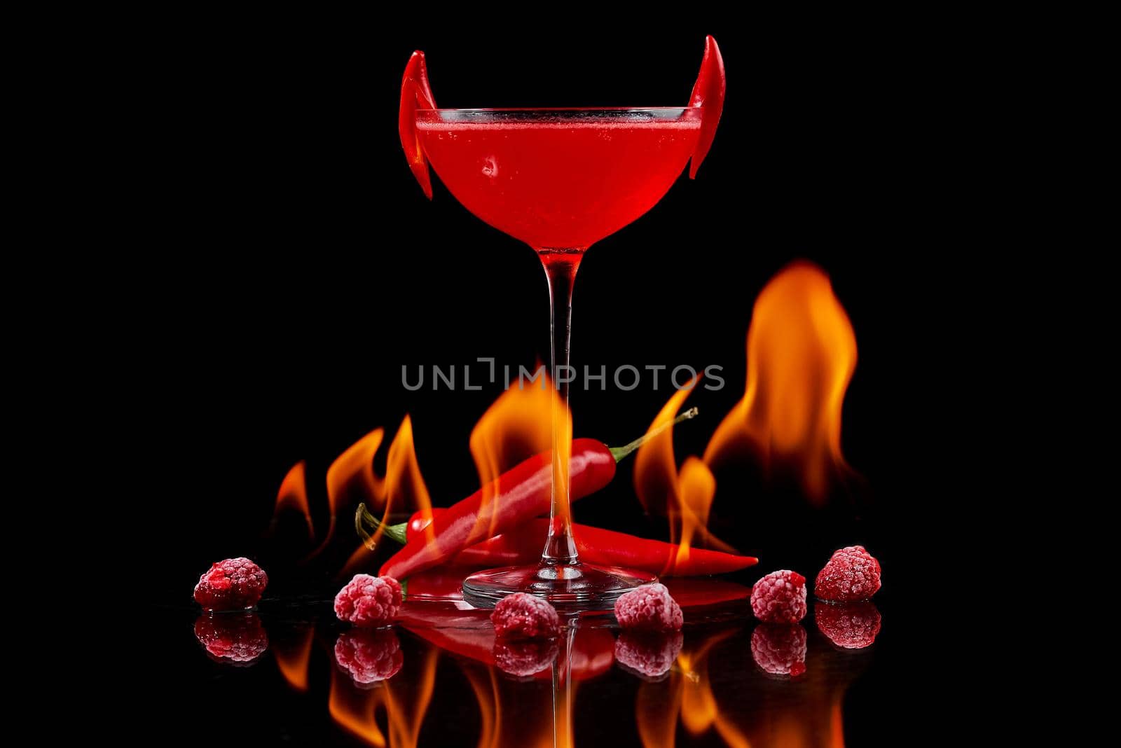 Red cocktail with raspberries and searing pepper on the mirror with flames of fire. High quality photo