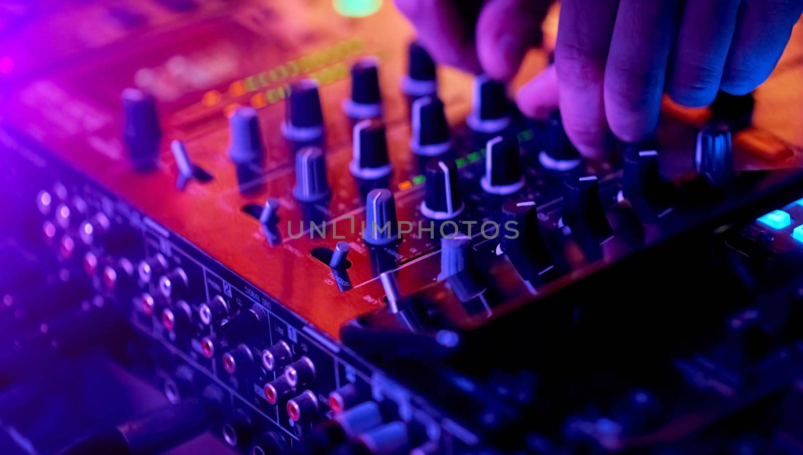 Hands of DJ mixing tracks on professional sound mixer..Closeup,knobs and regulators in focus. High quality photo