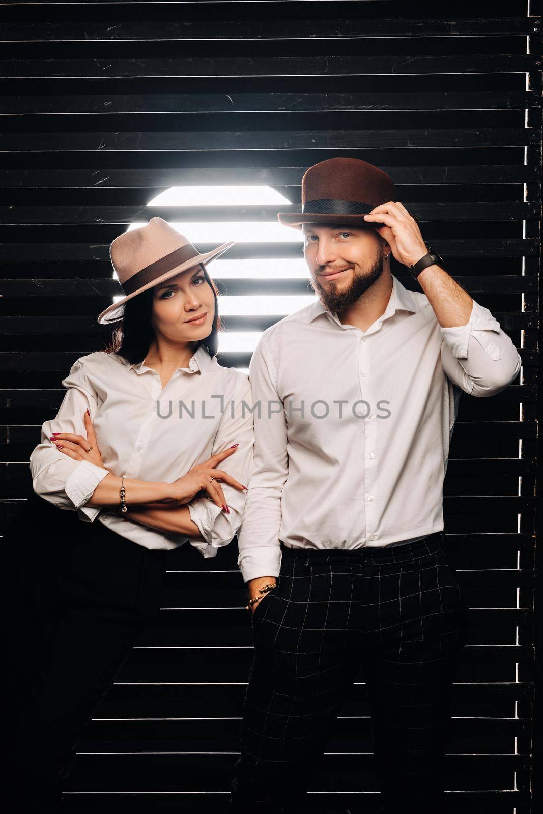 A man and a woman in white shirts and hats on a black background.A couple in love poses in the interior of the studio by Lobachad