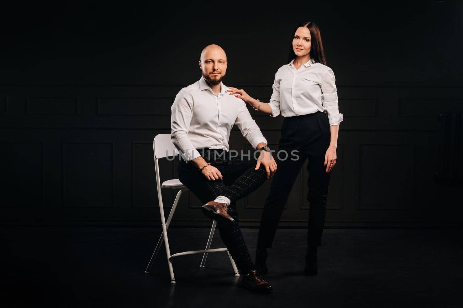 A man and a woman in white shirts on a black background.A couple in love in the studio interior by Lobachad