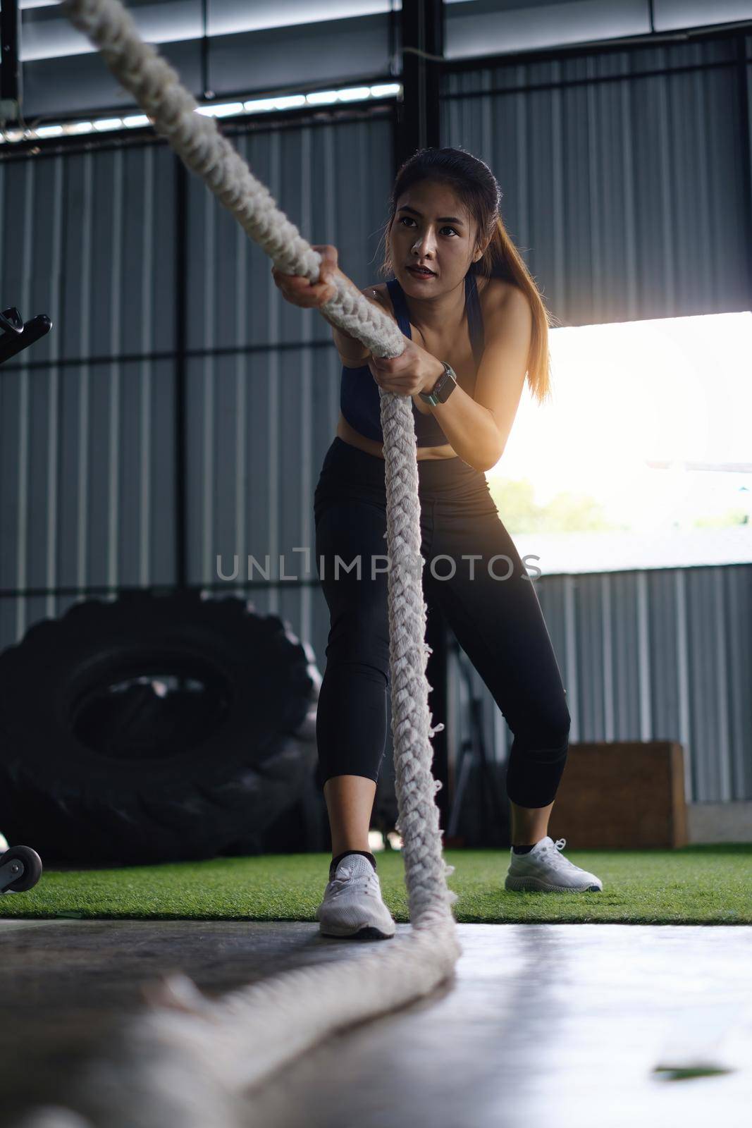 Female working out with battling rope at gym. Healthy modern people concept.
