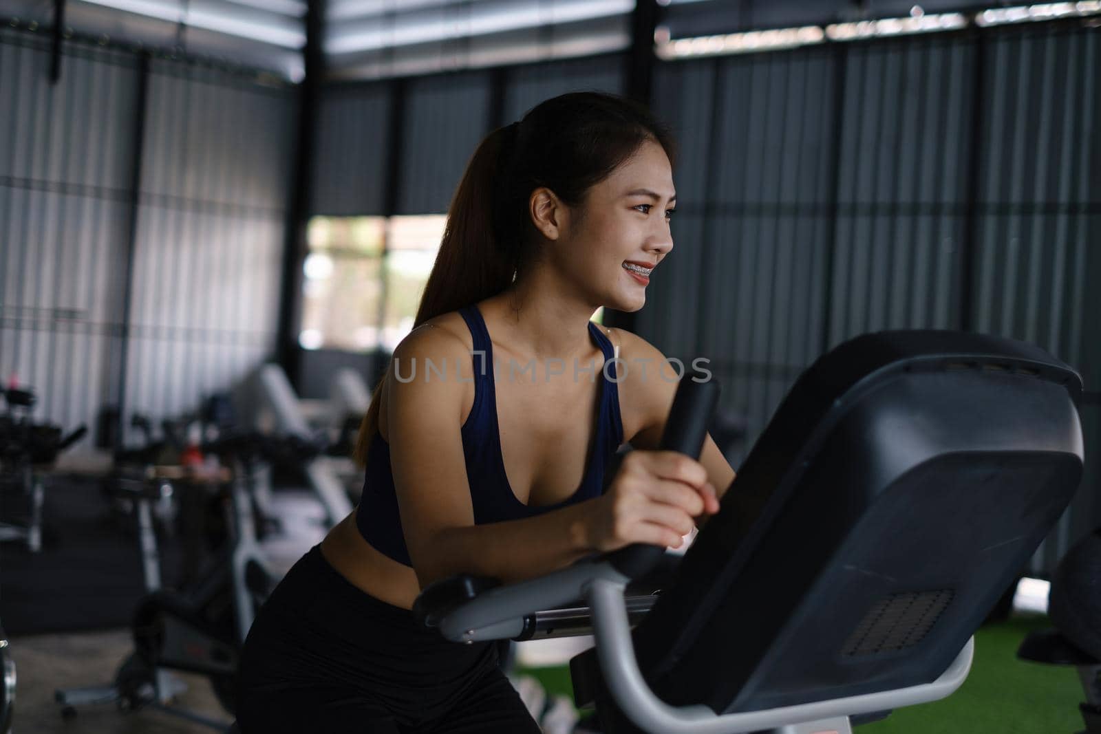 Happy young woman smiling and working out with sport biking fitness at class against fitness interface by itchaznong