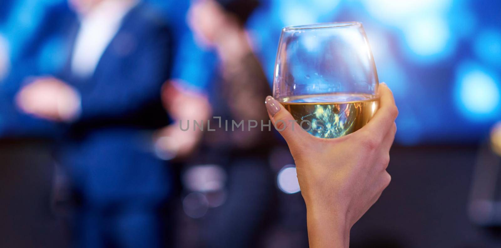 woman hand take up vine glass with persons blurred on background by AntonIlchanka