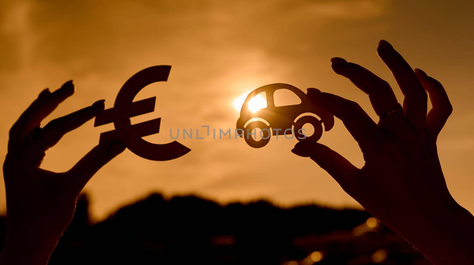 Euro symbol and car in women's hands contoured at sunset. High quality photo