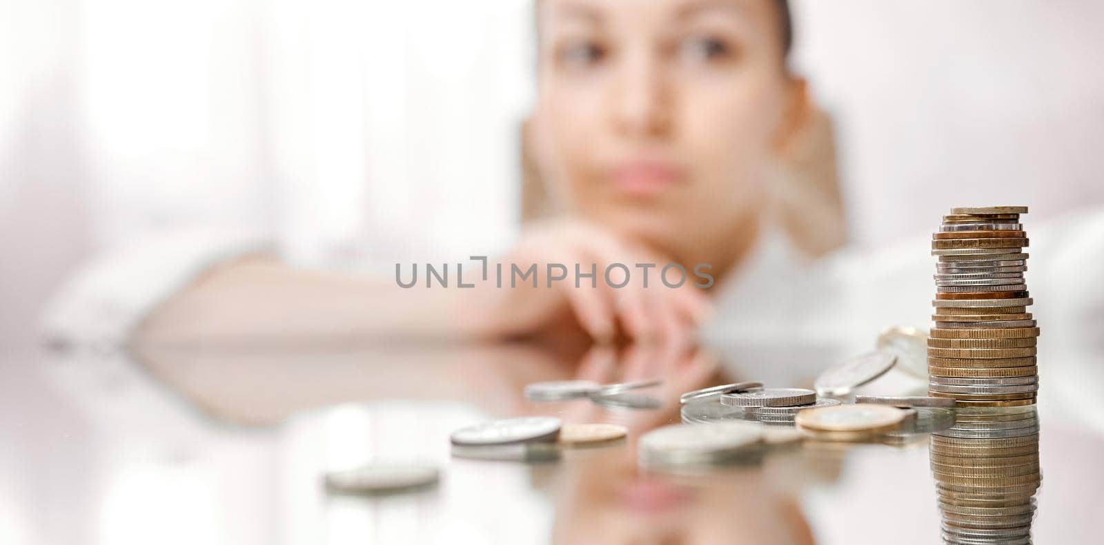 A woman looks thoughtfully at a fallen stack of coins on a mirrored table . High quality photo