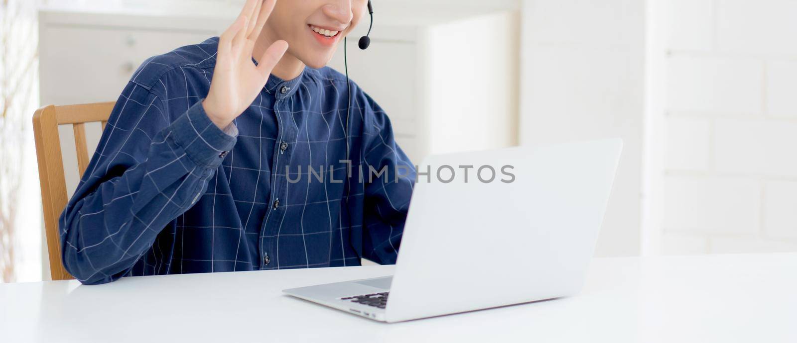 Young asian businessman working on laptop computer wearing headphone at home, business man wearing headset for video conference, communication and education, male study and learning for e-learning. by nnudoo