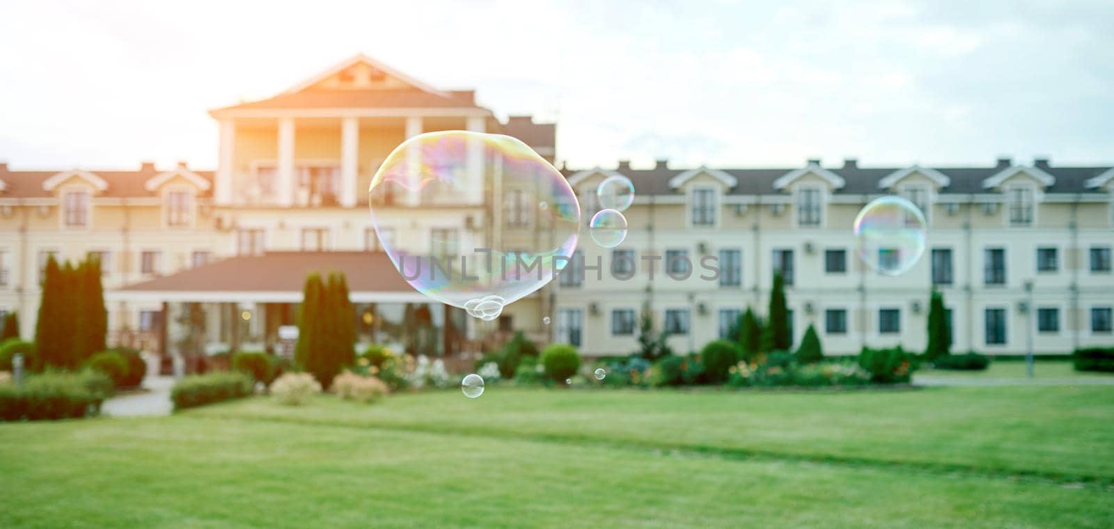 beautiful soap bubbles fly in front of a blurry respectable house with a park . High quality photo