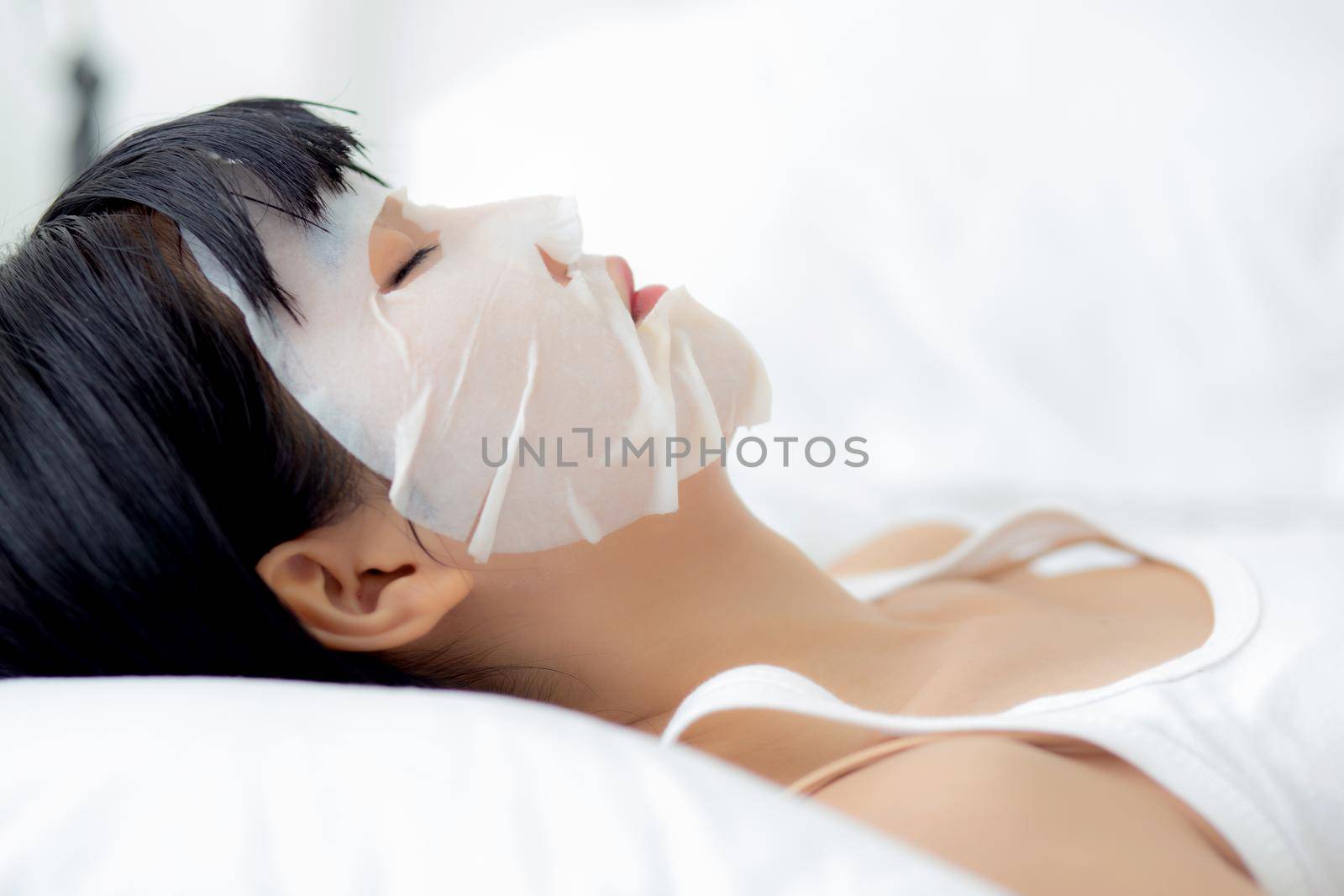 Beautiful young asian woman with sheet facial mask and sleep on bed at bedroom, beauty girl applying cosmetic and makeup with skin care face for wrinkle, skincare treatment, health and wellness. by nnudoo