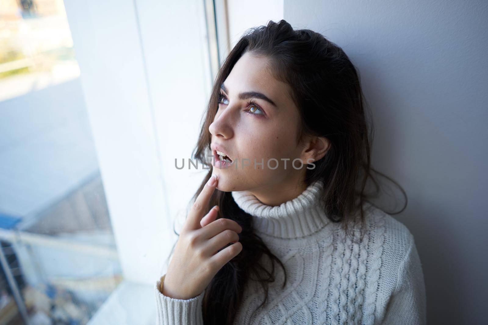 brunette in a white sweater looks out the window depression. High quality photo