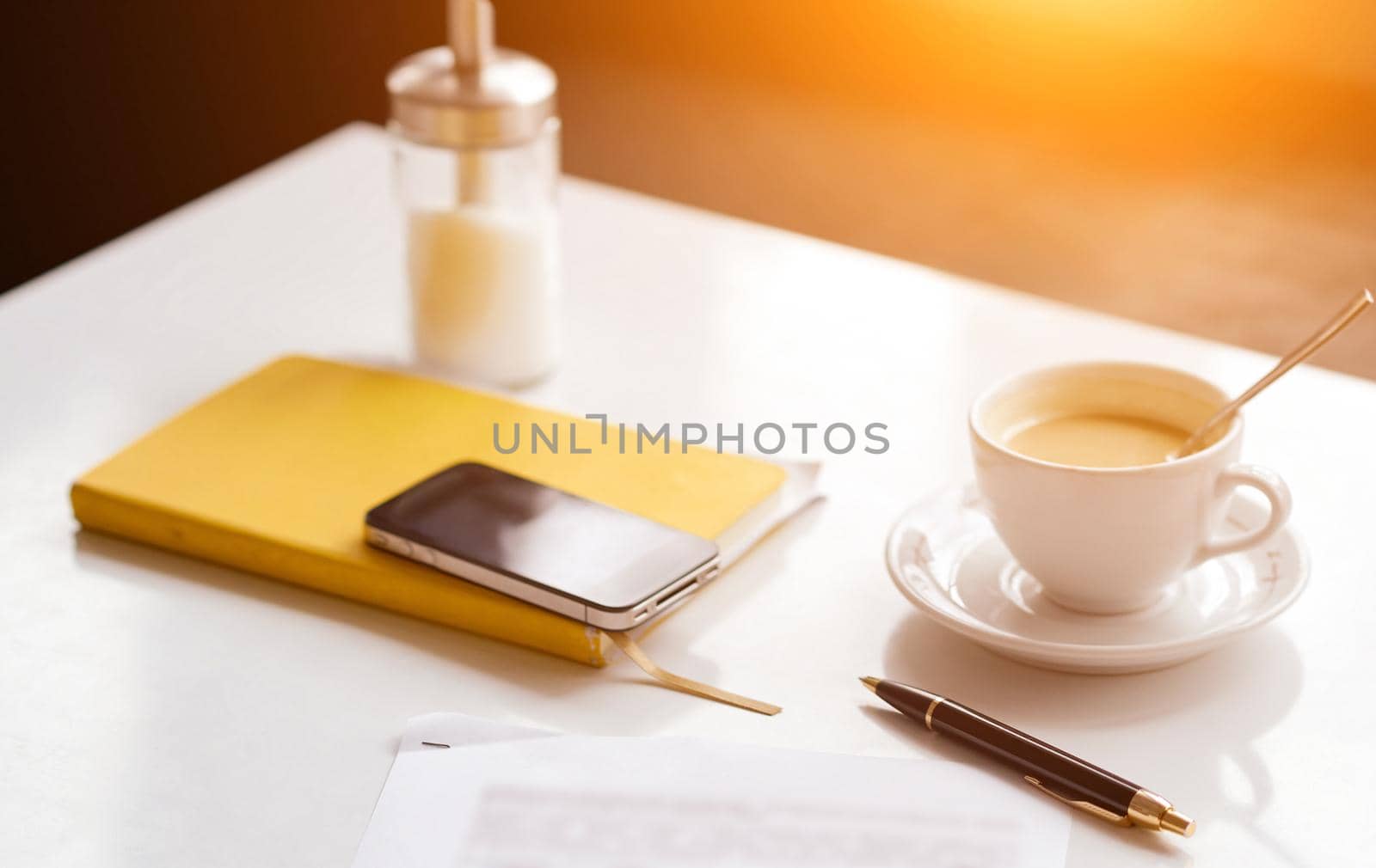 on the white table yellow notepad phone cup coffee pen and sheet of paper with a blurry dough . High quality photo