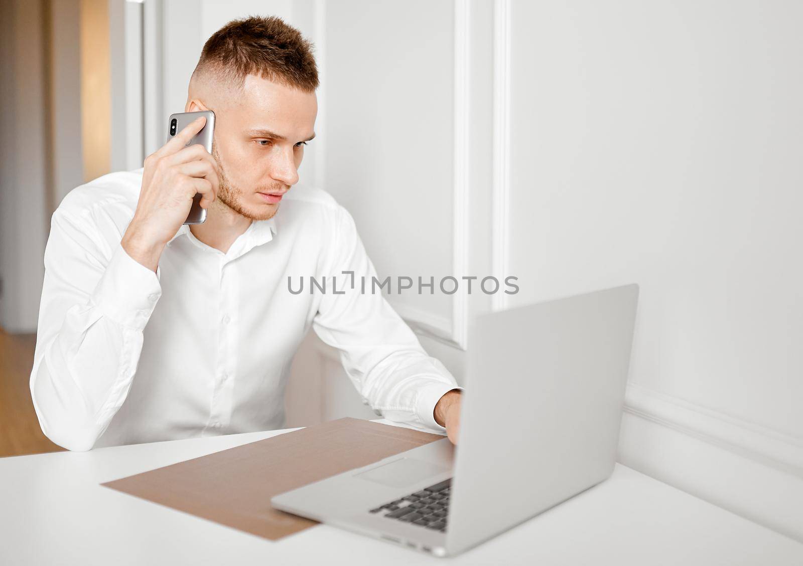 A young man works at home in the kitchen behind a laptop talking on the phone. High quality photo