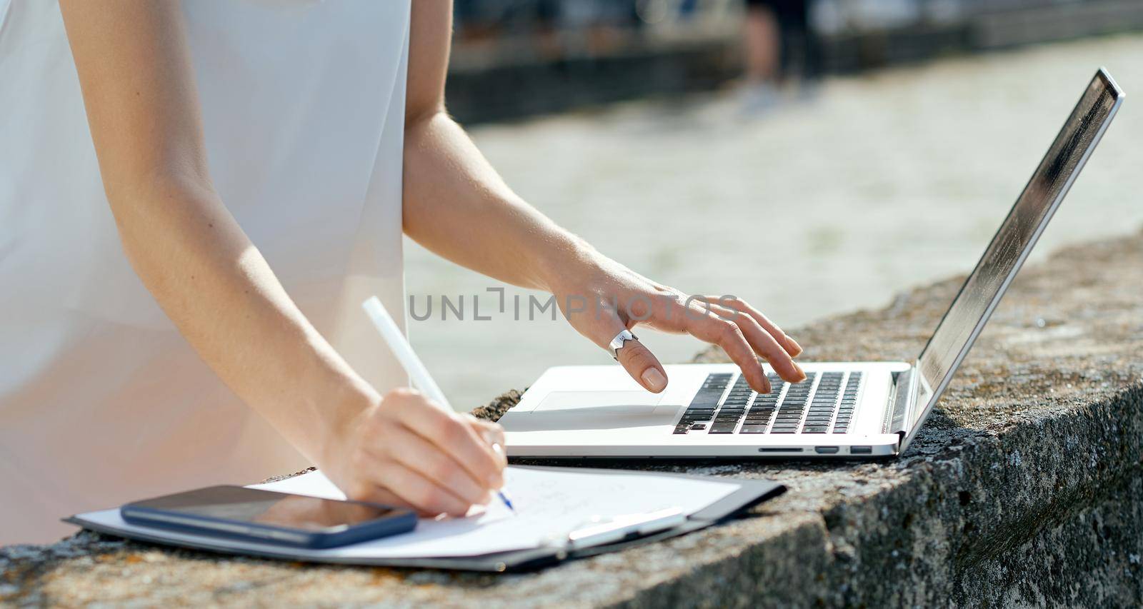 beautiful, serious girl in a white dress with a tablet, pen, laptop phone on the dock. High quality photo