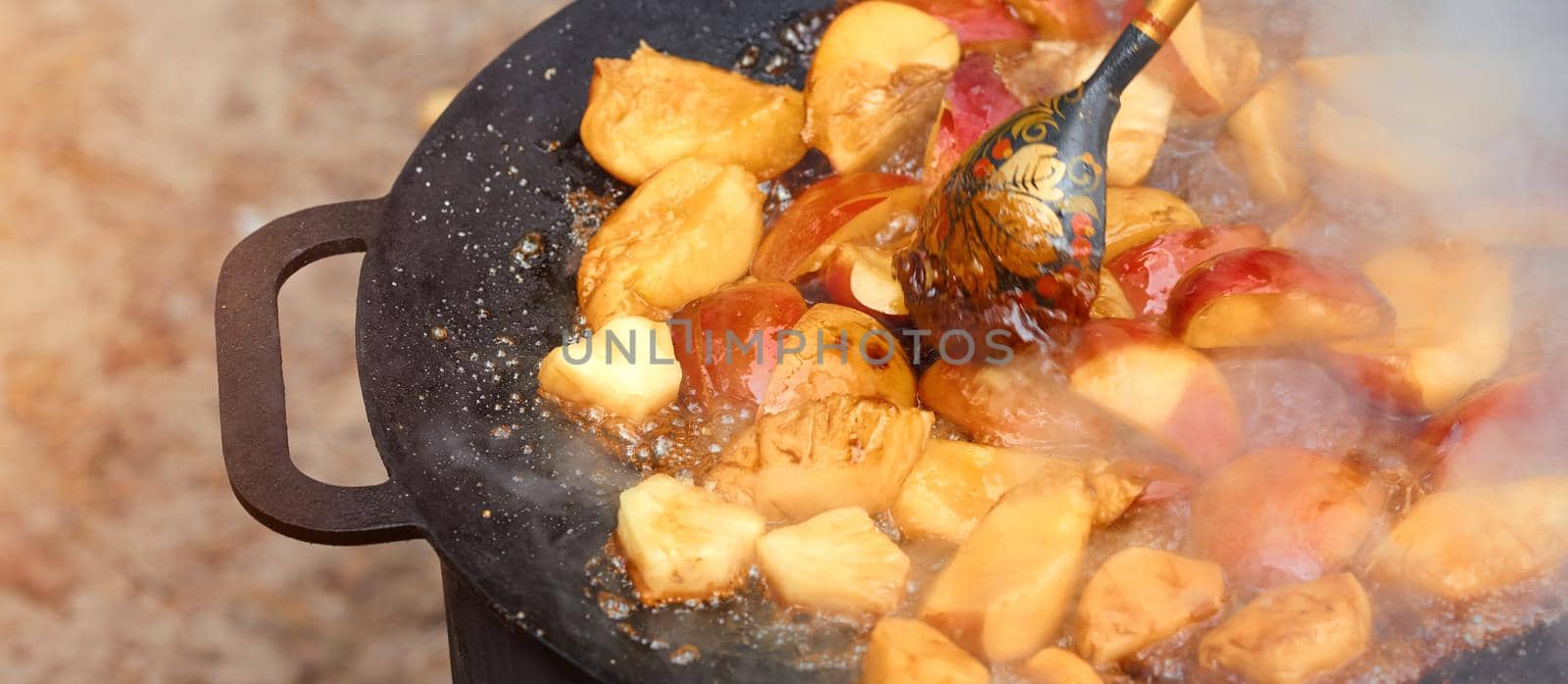 Fried apples in a cast-iron black frying pan on nature with wood spoon with Russian ornament . High quality photo