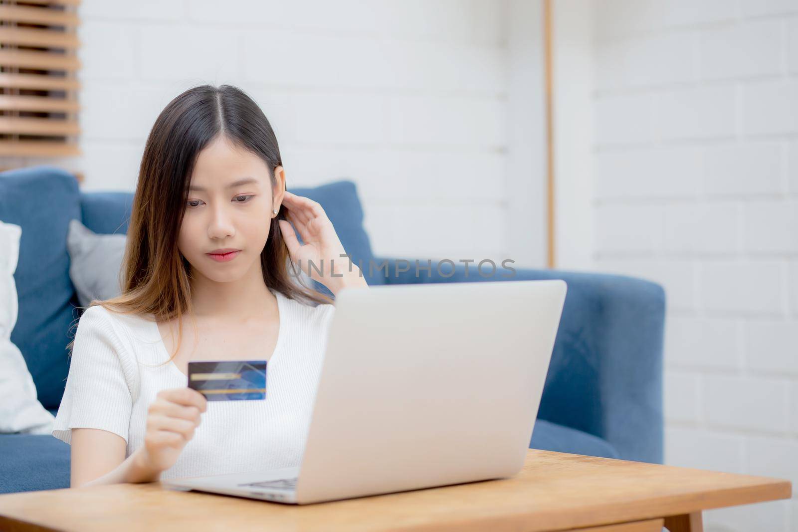 Young asian woman sit on sofa using laptop computer shopping online with credit card buying to internet, happy girl payment with e-business on couch, purchase and payment, business concept.