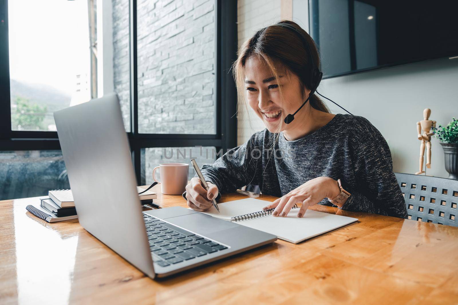 Happy asian woman student watching lesson online and studying from home. Young woman taking notes while looking at computer screen following professor doing math on video call.